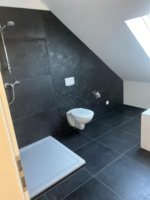 Fertiges Bad mit anthrazitfarbenen Großformatfliesen, Sechseck-Mosaik und Dachfenster