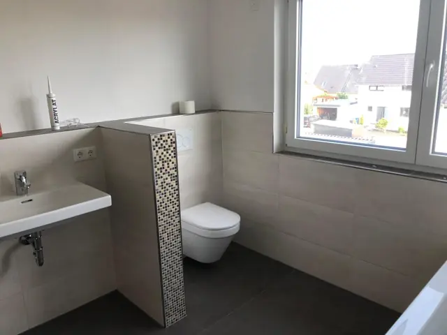 Bad mit beigen Großformatfliesen und Mosaikstreifen an der Vorwand