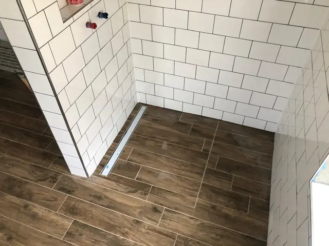 Dusche mit weißen Metrofliesen und Holzoptik-Boden mit Rinne