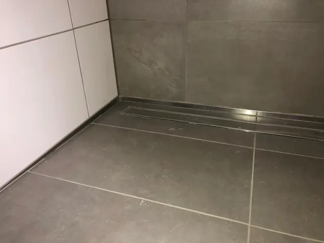 Duschbereich mit Entwässerungsrinne und grauen Großformatfliesen