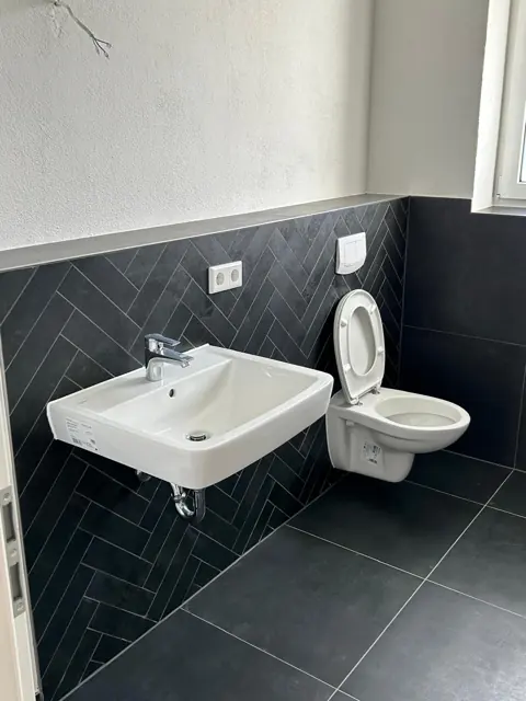 Waschtisch und WC vor einer Wand im Fischgrätmuster