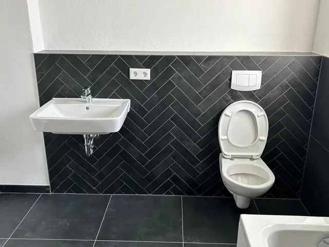 Wand-WC und Waschbecken vor anthrazitfarbenen Fliesen im Fischgrätmuster